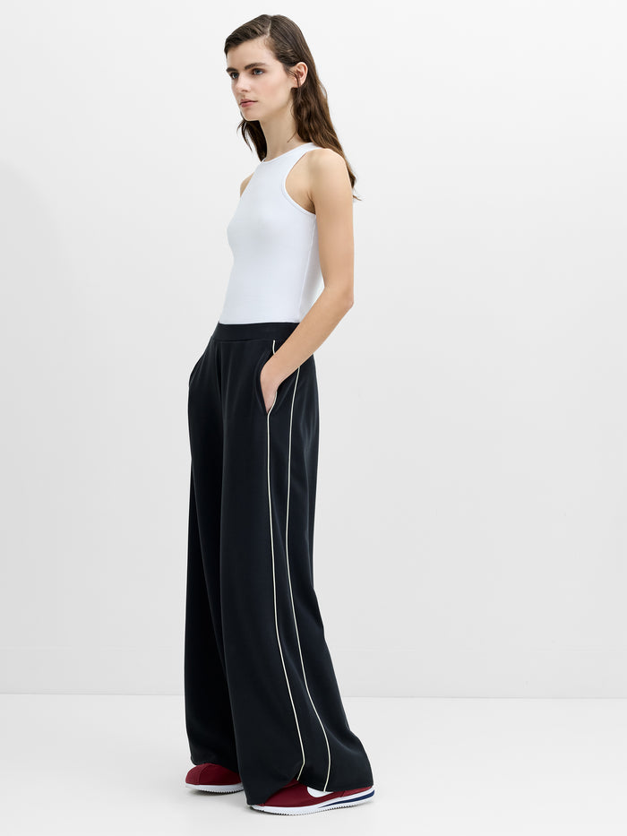 A woman wearing dark grey wide leg joggers with side stripes, a soft fabric finish, a high rise elasticated waistband, and side pockets.