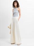 A woman wearing wide leg, full length porcelain cream trousers with an elastic waistband and two pockets.