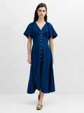 A woman wearing a flowing, midi length navy blue dress with a V-neck, flutter sleeves and an empire waistline with button down fastening.