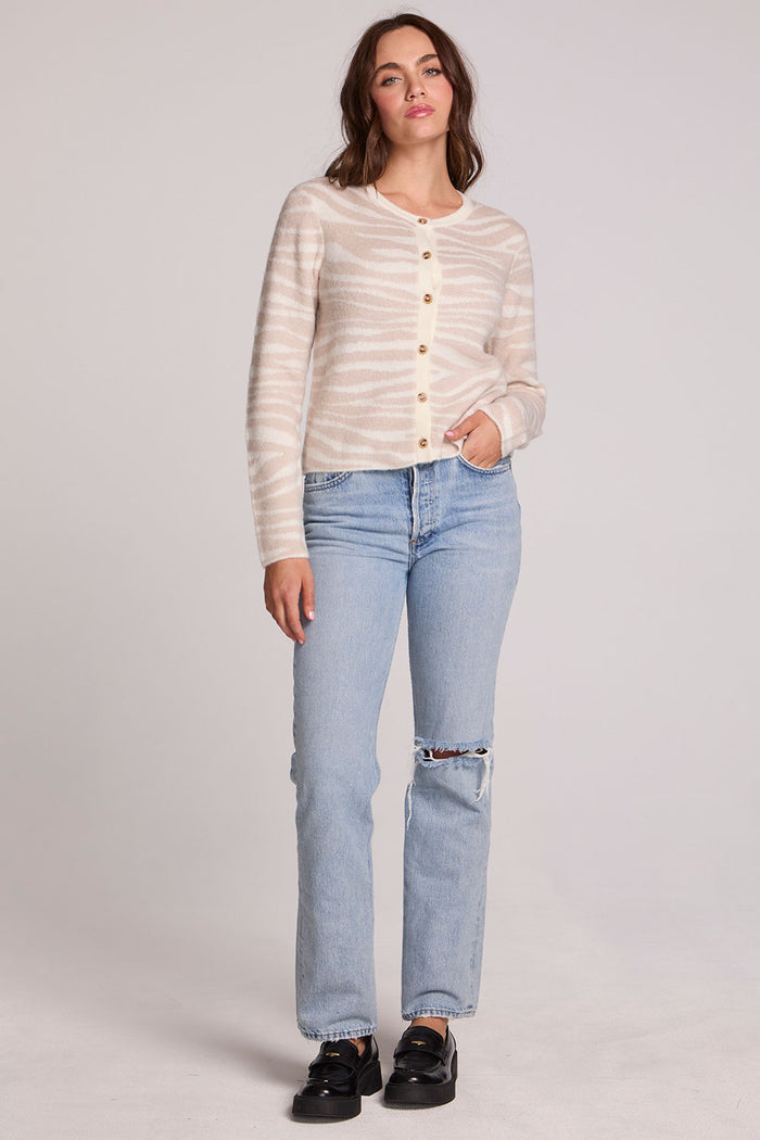 Full body front view of a woman wearing the Chaser  Zebra Dream Striped Cardigan and jeans on a neutral background with one hand in pocket