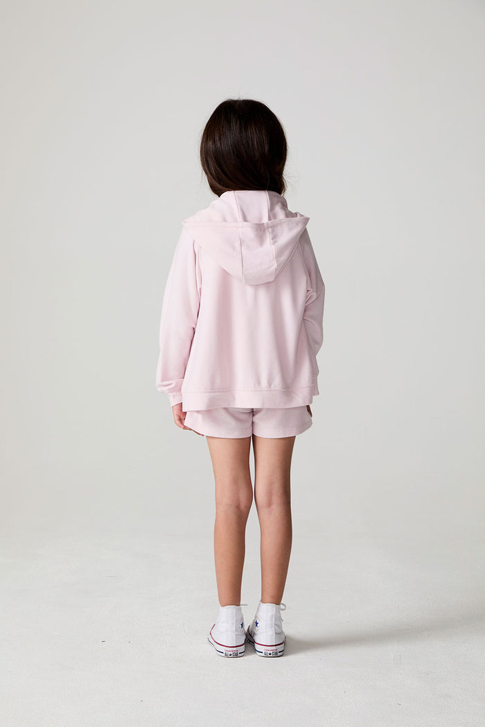 Back view of a girl wearing the Chaser Zip Up Begonia Hoodie on a neutral background